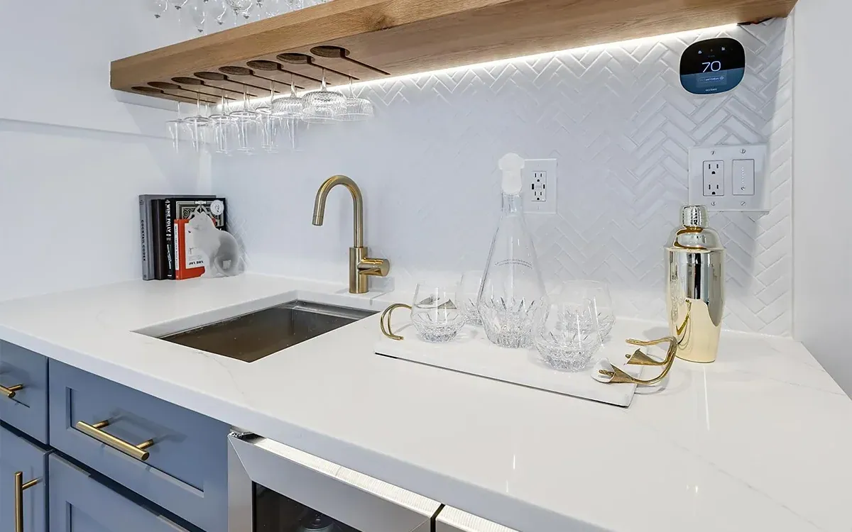 Wet bar with blue cabinetry, white oak shelf with glass holders and brass tap